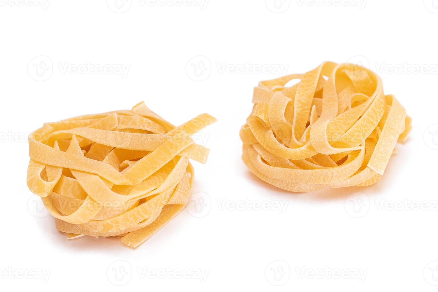 Two Classic Italian Raw Egg Fettuccine - Isolated on White Background. Dry Twisted Uncooked Pasta. Italian Culture and Cuisine. Raw Golden Macaroni Pattern - Isolation photo