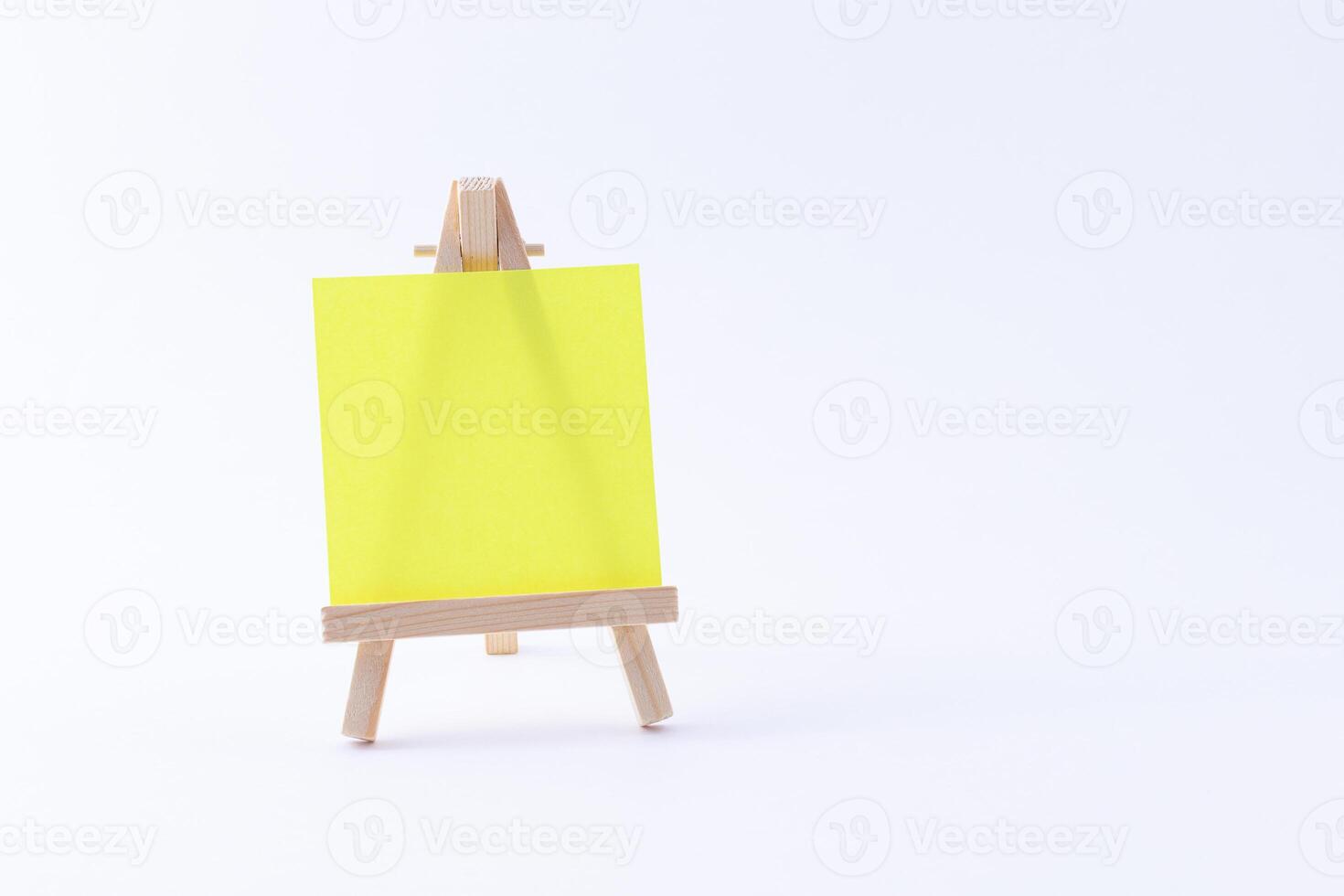 Wooden Easel Miniature with Blank Colored Square Canvas or Memo Paper - Mockup. Mini Wooden Stand with Clean Artboard on White Background, Copy Space photo