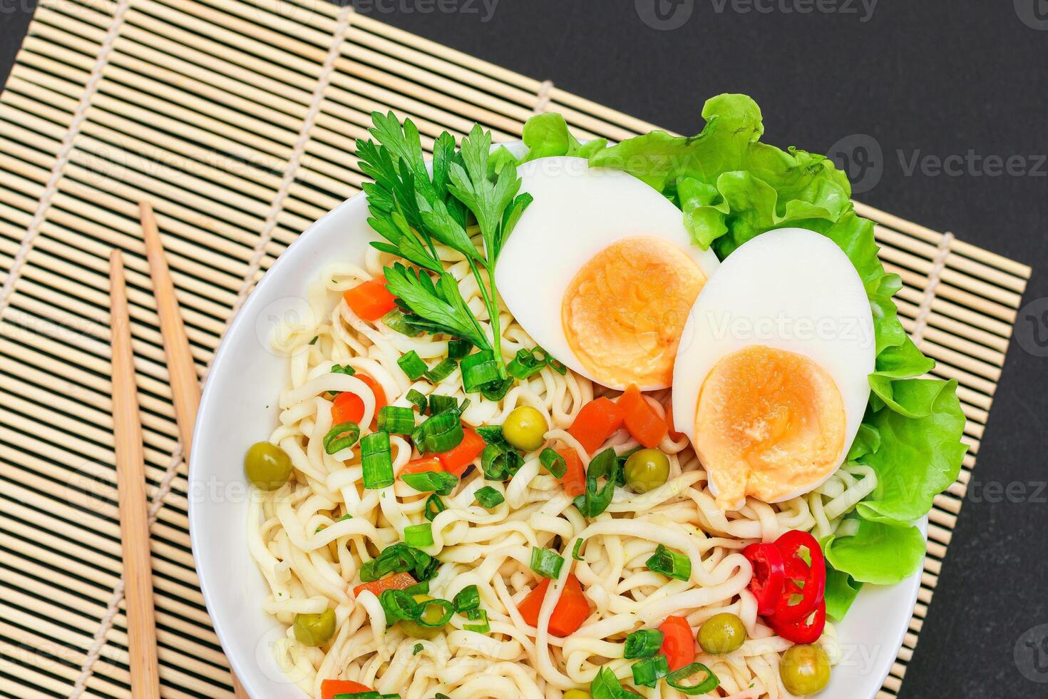 Beautiful Noodle Dish with Green Pea, Carrot, Eggs, Red Hot Pepper and Greens on Sushi Mat. Instant Noodles with Vegetables photo