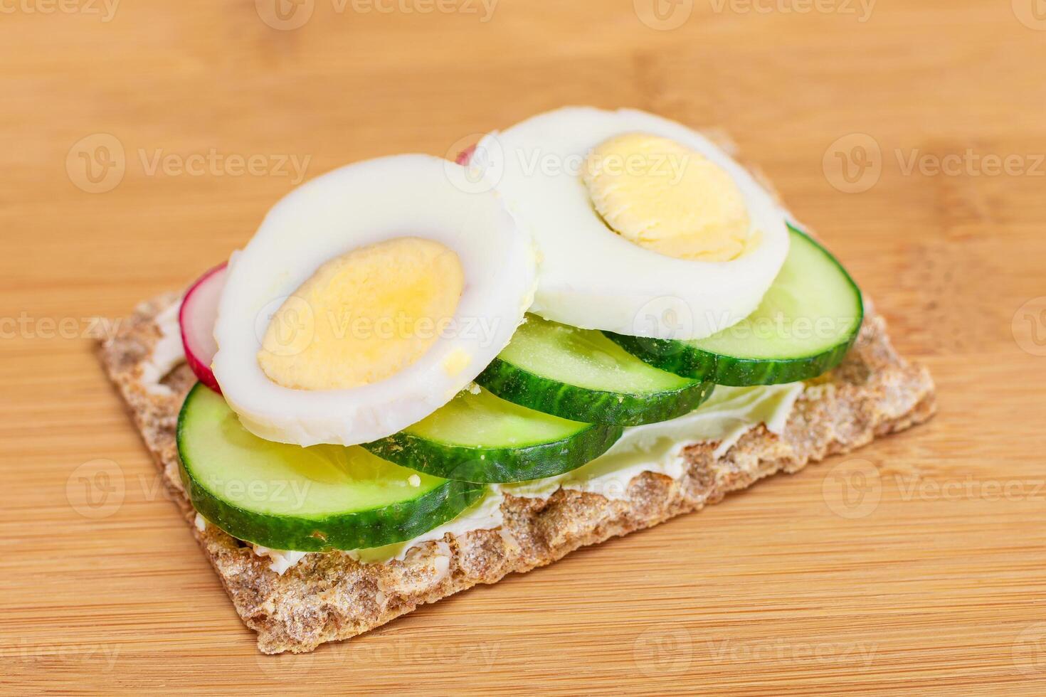 Whole Grain Crispbread with Fresh Cucumber, Egg, Cream Cheese and Radish on Bamboo Cutting Board. Easy Breakfast. Quick and Healthy Sandwiches. Crispbread with Tasty Filling. Healthy Dietary Snack photo