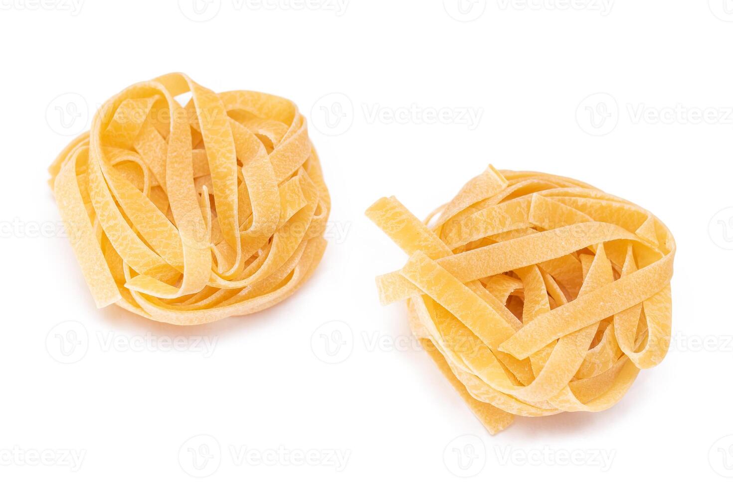 Two Classic Italian Raw Egg Fettuccine - Isolated on White Background. Dry Twisted Uncooked Pasta. Italian Culture and Cuisine. Raw Golden Macaroni Pattern - Isolation photo