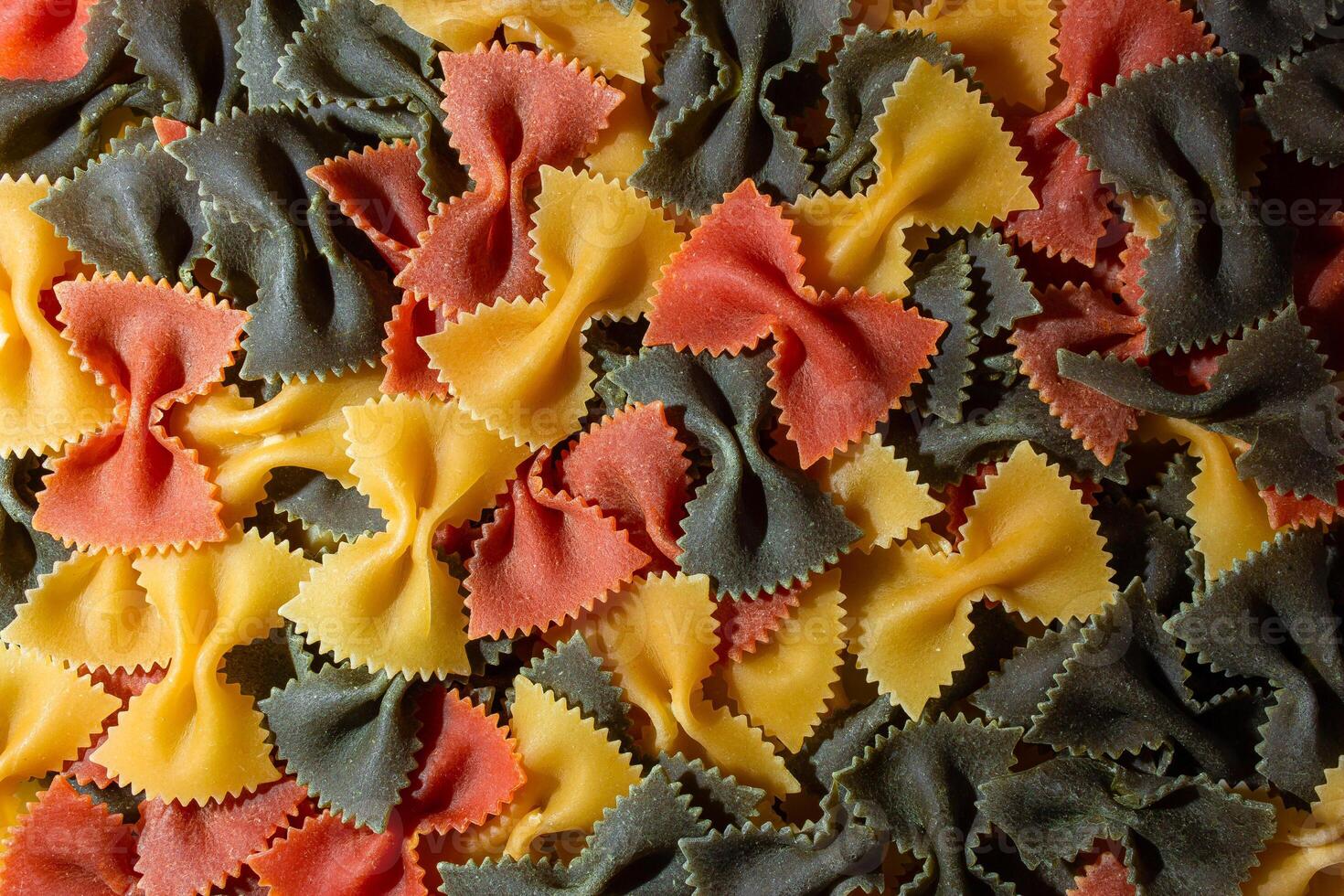 Uncooked Vibrant Colored Farfalle Pasta. A Culinary Canvas of Multicolored Bow-Tie Macaroni, Creating a Lively and Textured Background for Gourmet Cooking Enthusiasts. Colored Dry Pasta. Raw Macaroni photo