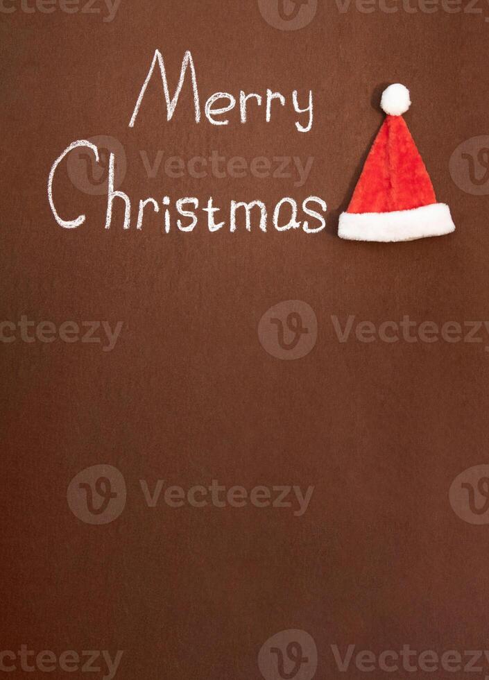 Merry Christmas handwritten in chalk, with Santa's hat nearby, on an abstract background. With space for text photo