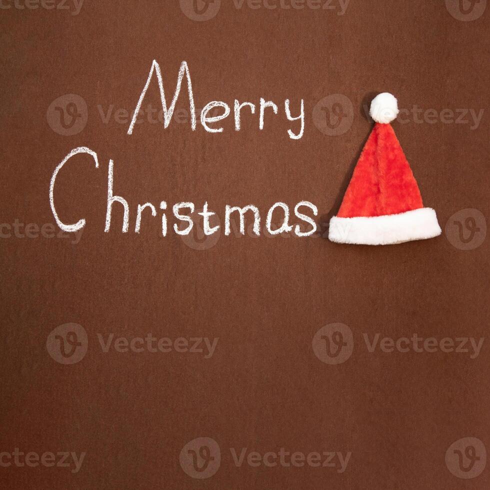 Merry Christmas handwritten in chalk, with Santa's hat nearby, on an abstract background. With space for text photo