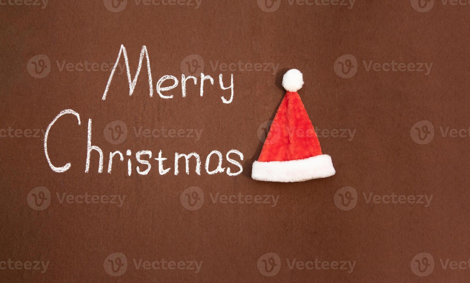 Merry Christmas handwritten in chalk, with Santa's hat nearby, on an abstract background. With space for text photo