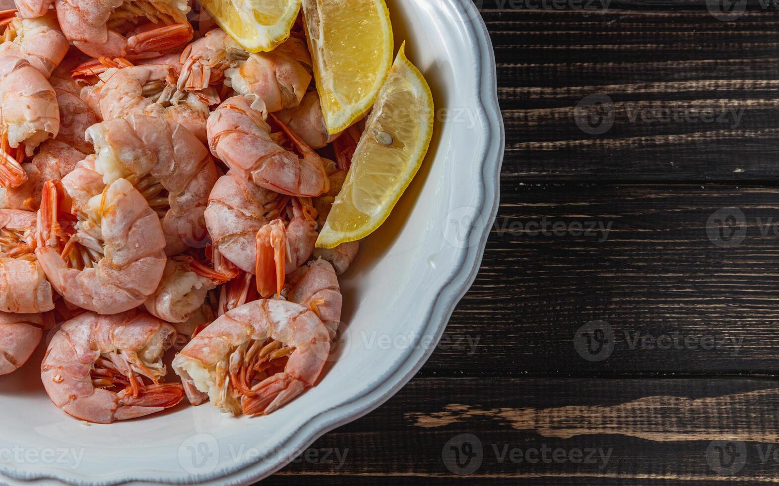 Boiled king prawns in deep bowl with lemon close up view on dark table photo