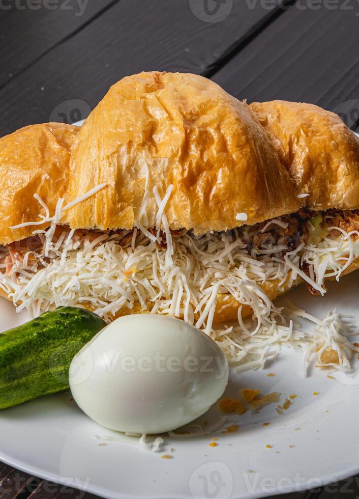 Croissant sandwich with tuna, egg and cucumber on a white plate on a dark table photo