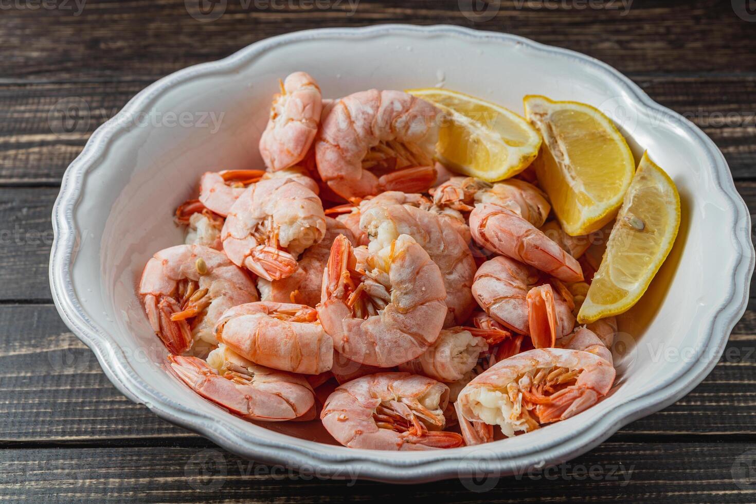 Boiled king prawns in deep bowl with lemon close up view on dark table photo