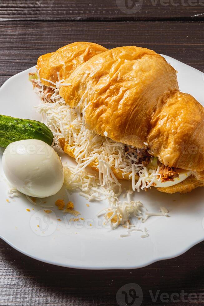 Croissant sandwich with tuna, egg, cucumber and cheese on a white plate photo