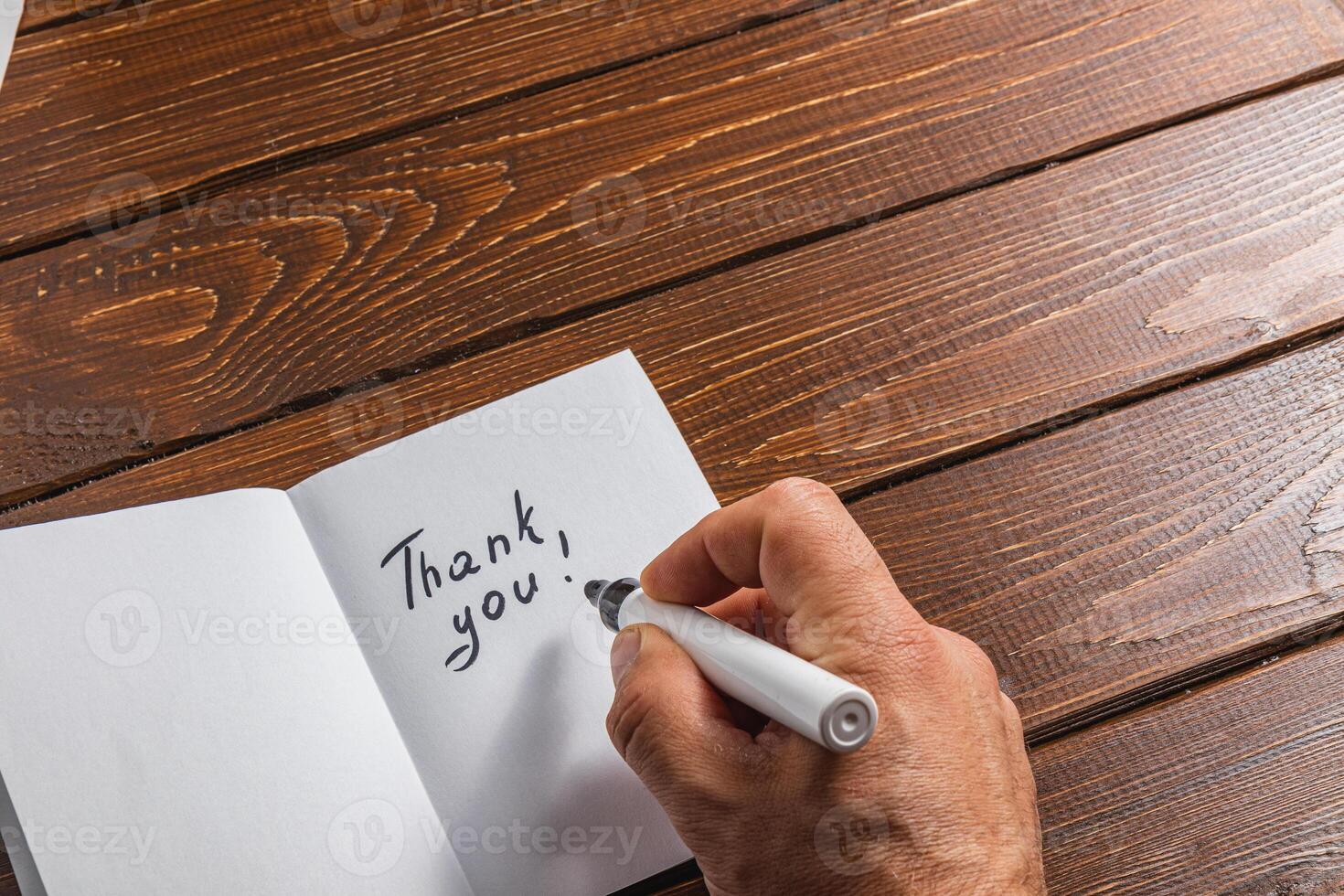 A person is writing a thank you note on a piece of paper on a wooden table photo