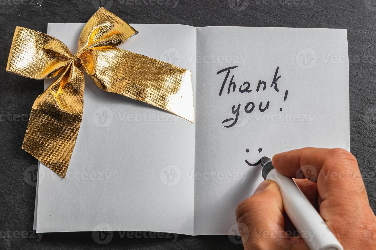 A man writes thank you on an open piece of paper with a golden bow photo