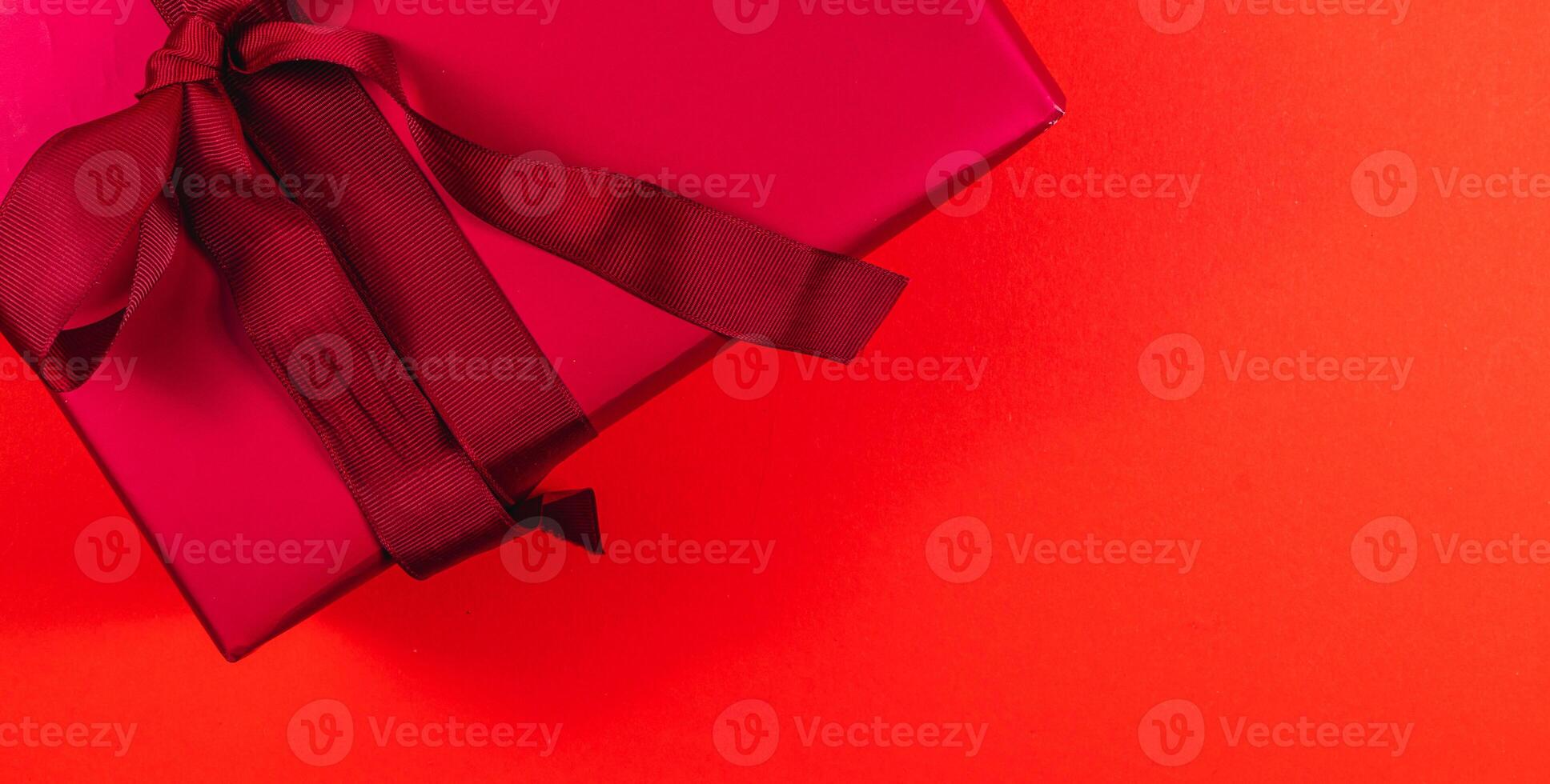 banner Red gift box with dark red bow and ribbon on red background photo