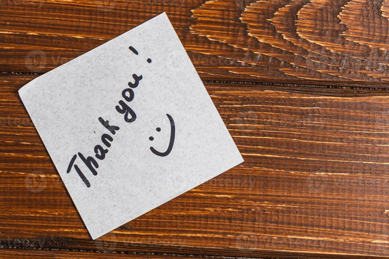 A thank you note is written on a piece of paper and placed on a wooden surface. photo