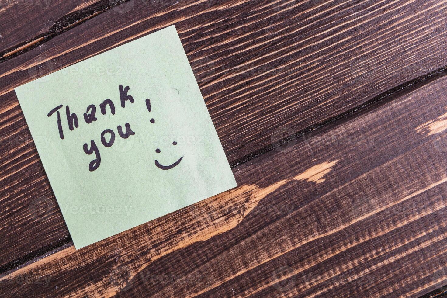 A thank you note is written on a piece of paper and placed on a wooden surface. photo