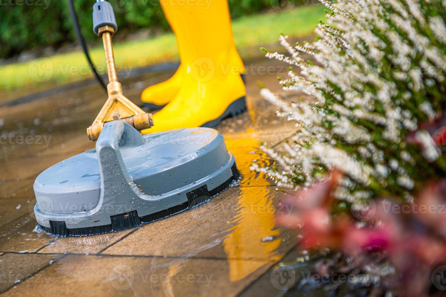 Pressure Washer Cleaning Patio Tiles With a Person in Yellow Boots on a Sunny Day photo