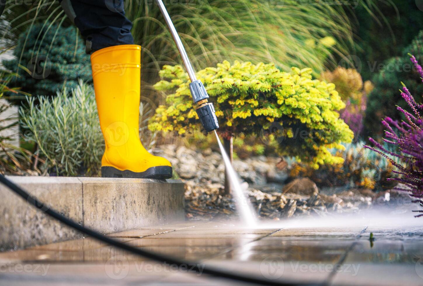 Person Cleaning a Patio With a Pressure Washer While Wearing Yellow Rubber Boots in a Garden photo