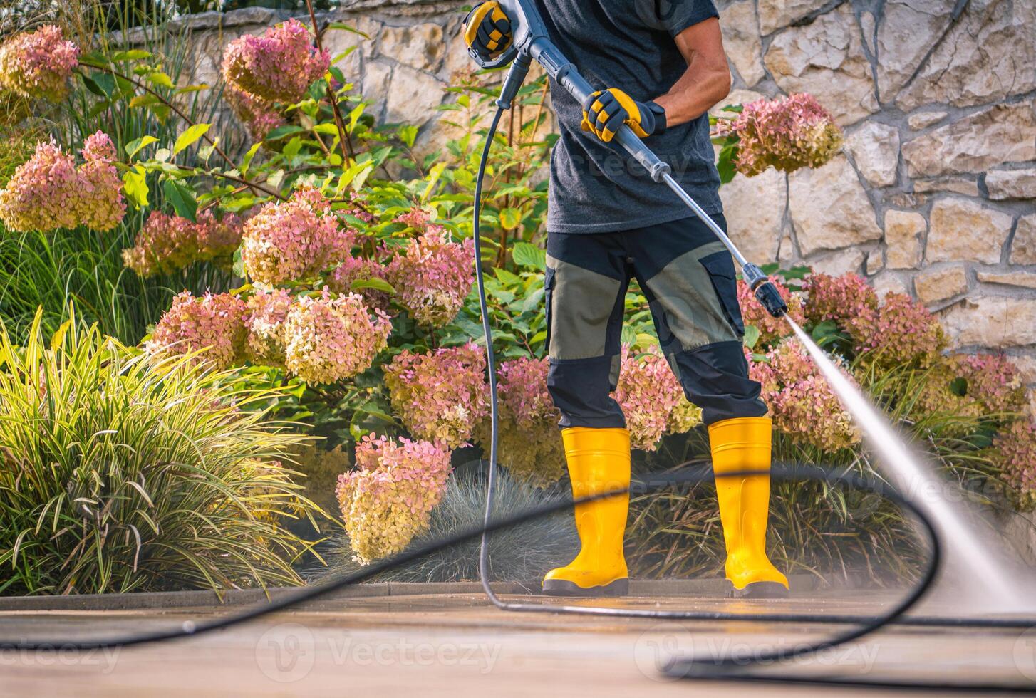 Person Using a Pressure Washer on a Patio Surrounded by Blooming Flowers During Daytime photo
