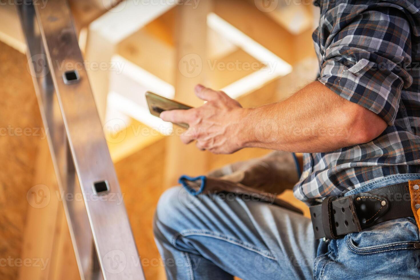 Worker Using a Smartphone While on a Ladder During Home Construction in a Light-Filled Workspace photo