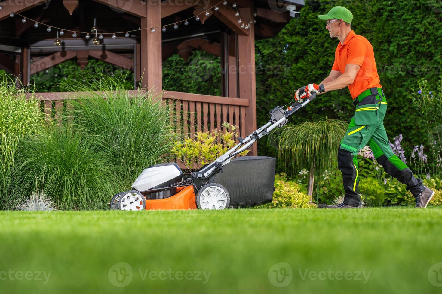 Professional Landscaper Mowing a Lush Green Lawn Near a Wooden Gazebo on a Sunny Afternoon photo