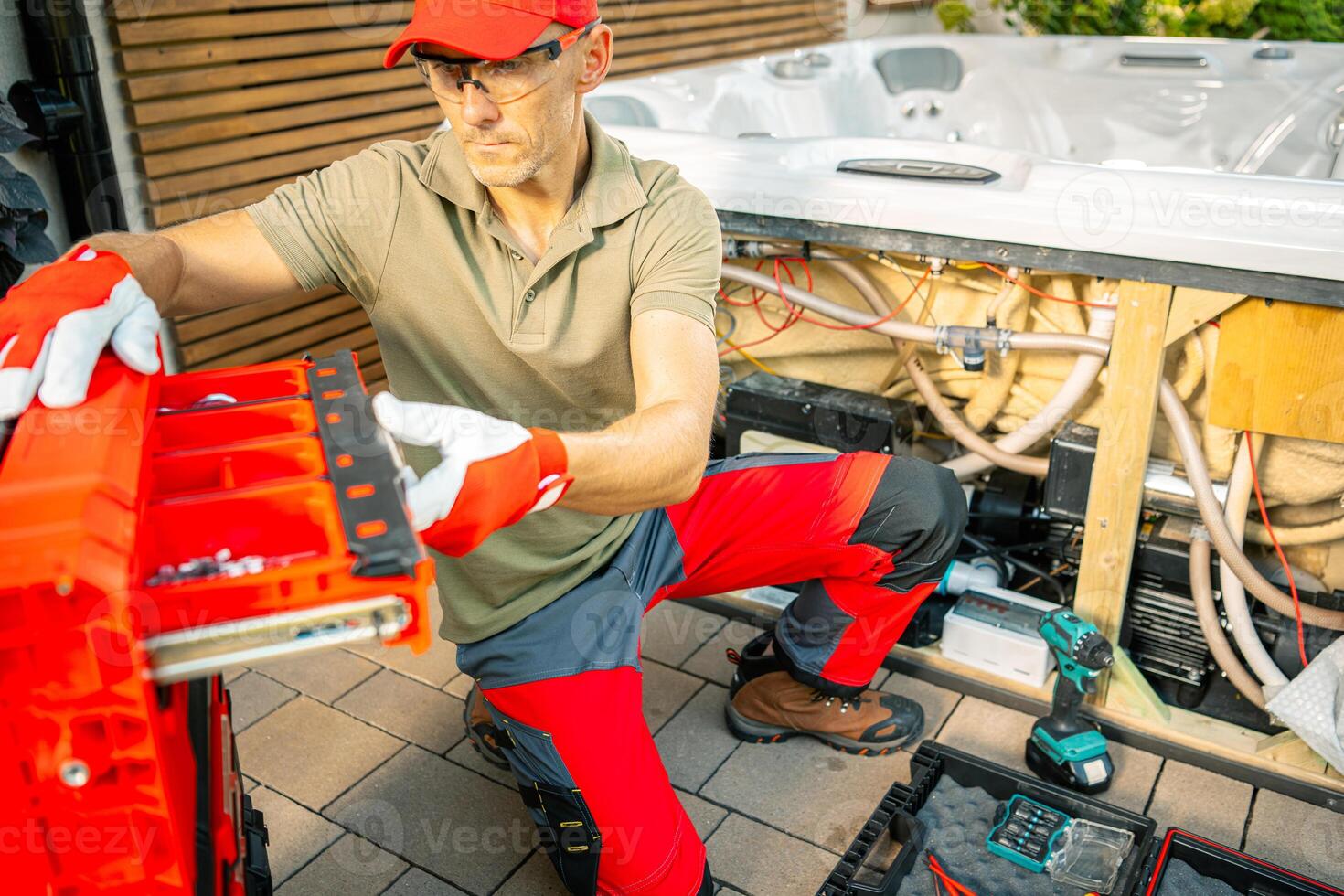 A Technician Repairs a Hot Tub With Tools While Kneeling on a Patio in a Residential Backyard photo