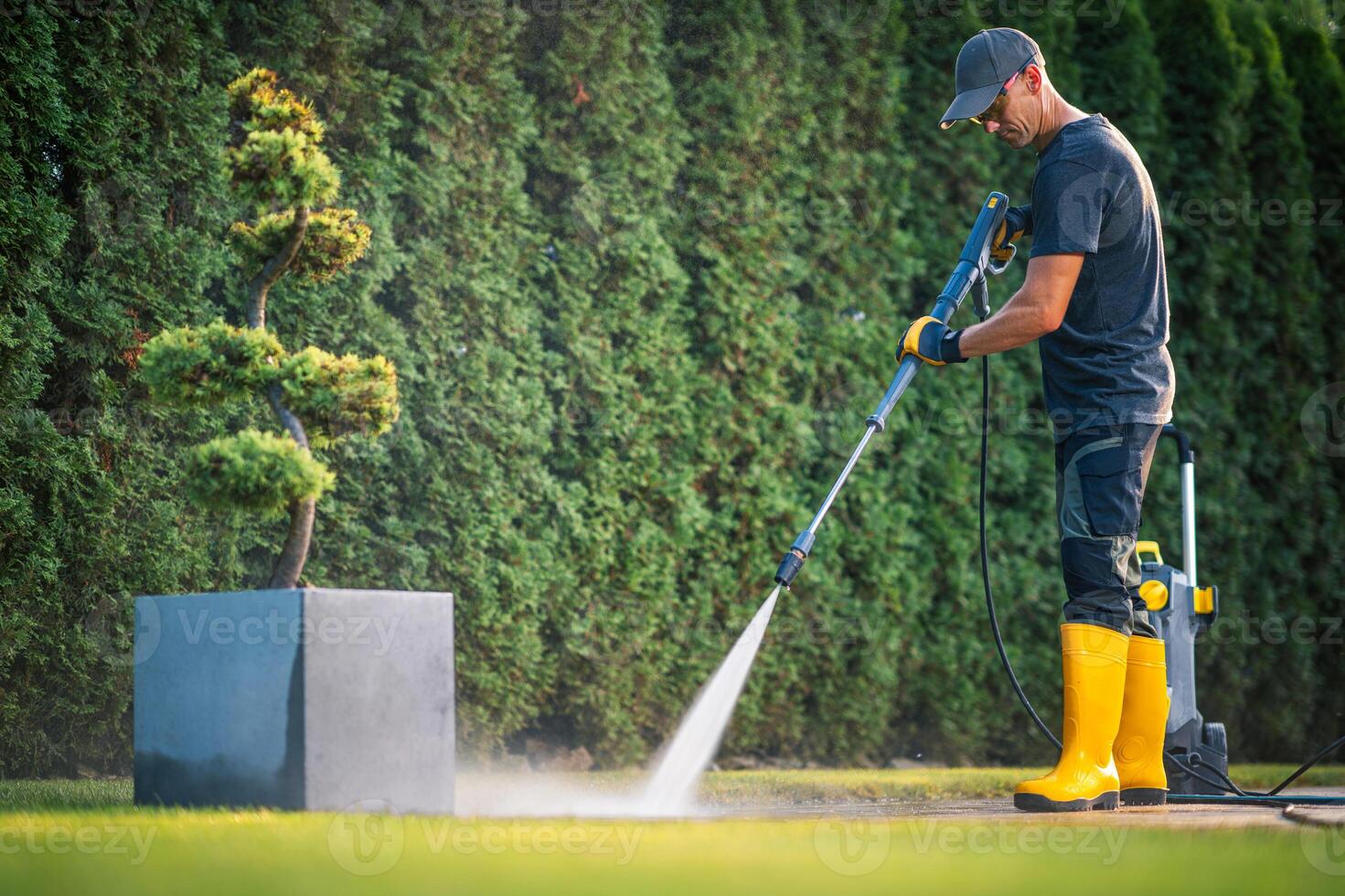 Professional Landscaper Using a Pressure Washer to Clean Garden Paths in a Residential Yard photo