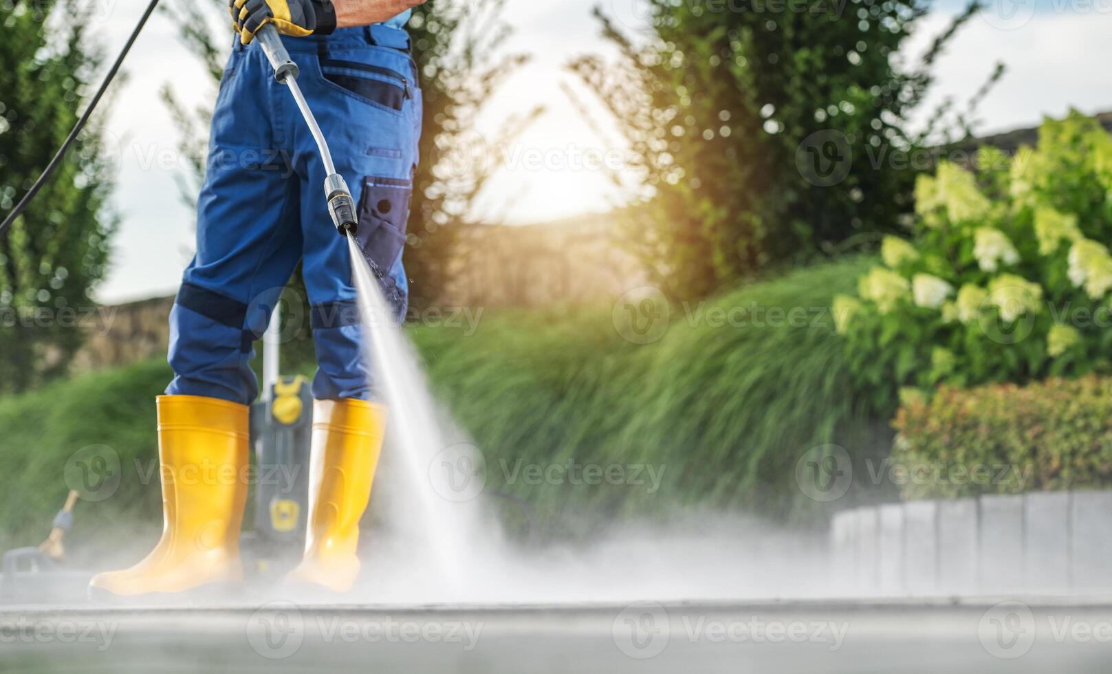 Man Using a Pressure Washer to Clean Outdoor Patio During Bright Sunny Day in a Landscaped Backyard photo