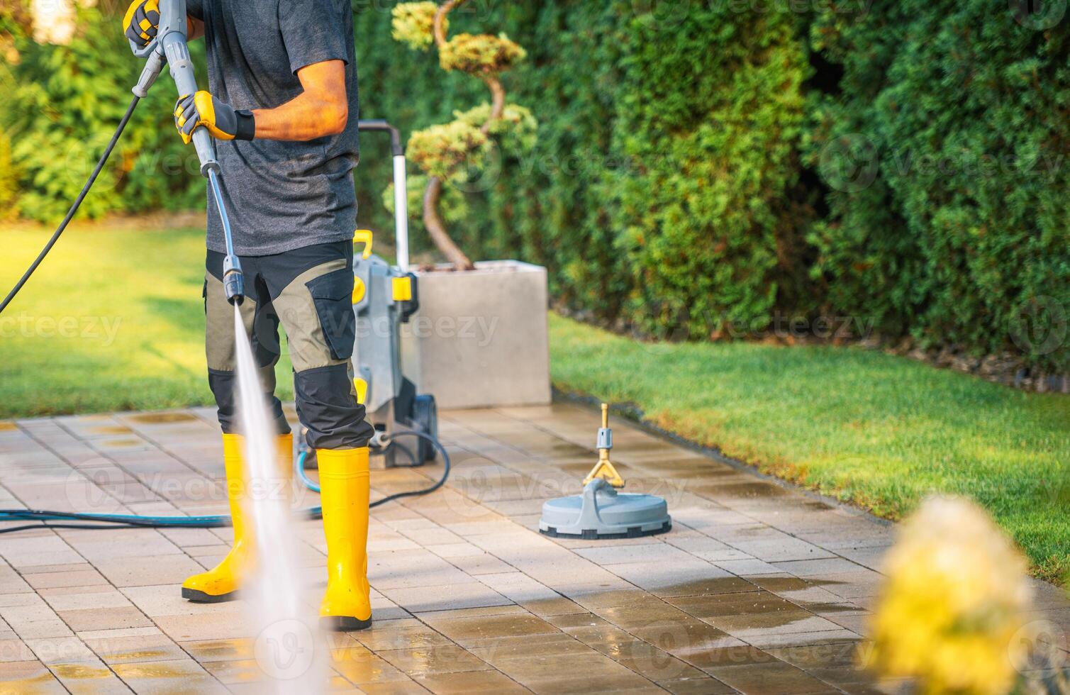 Person Pressure Washing a Patio in a Garden on a Sunny Day, Showcasing Clean Outdoor Surfaces photo