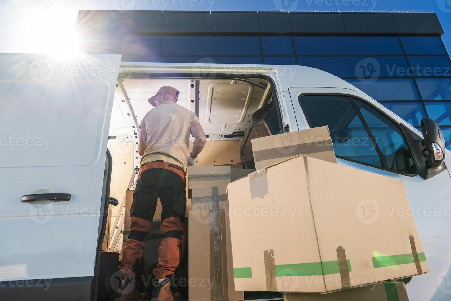 Delivery Worker Unloading Boxes From a Van in Bright Sunlight Outside a Modern Office Building photo