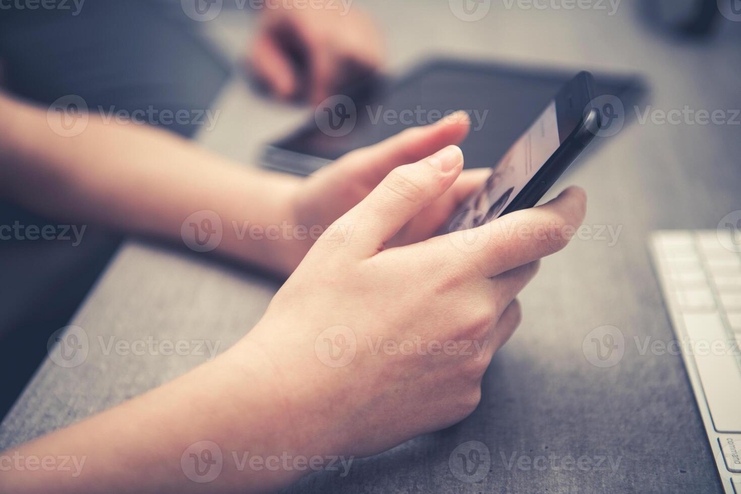 Person Using a Smartphone While Sitting at a Desk With a Tablet and Keyboard in a Modern Setting photo