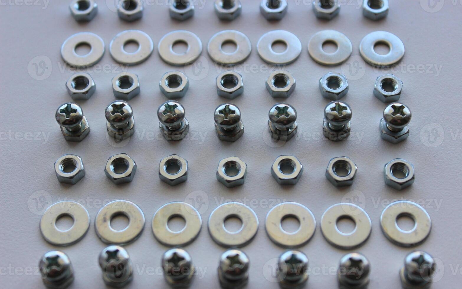 Perfectly even rows of steel shiny nuts, bolts and washers on a white surface photo