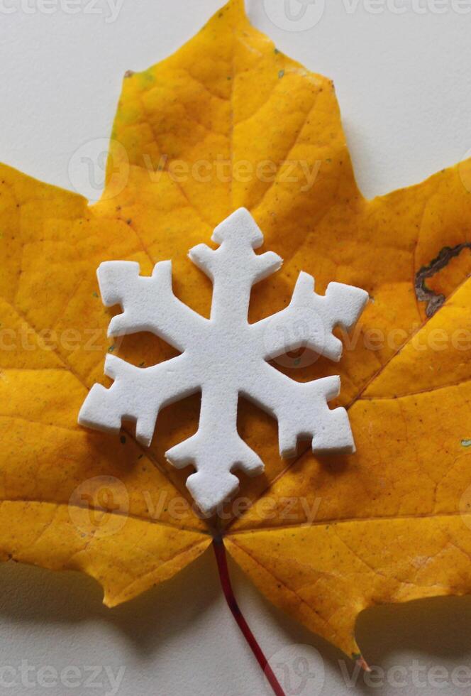 A toy snowflake covers a bright yellow autumn leaf. Symbols of the end of autumn and the beginning of winter photo