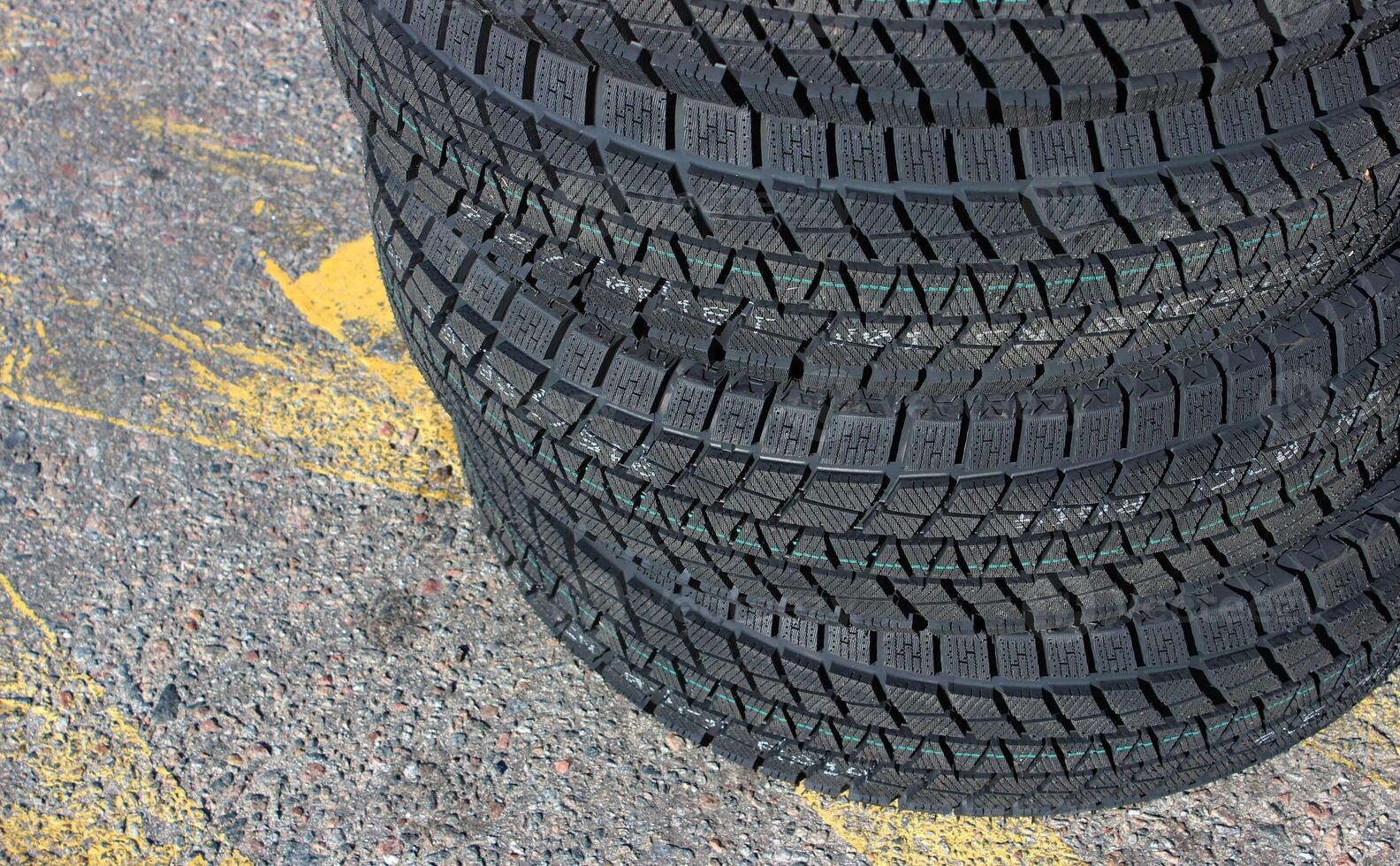 Identical winter tires with aggressive tread patterns are stacked on the highway. Same studless tires stock photo