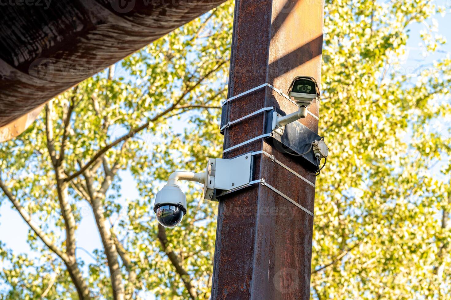 Two security cameras mounted on a rusty pole monitoring the area photo