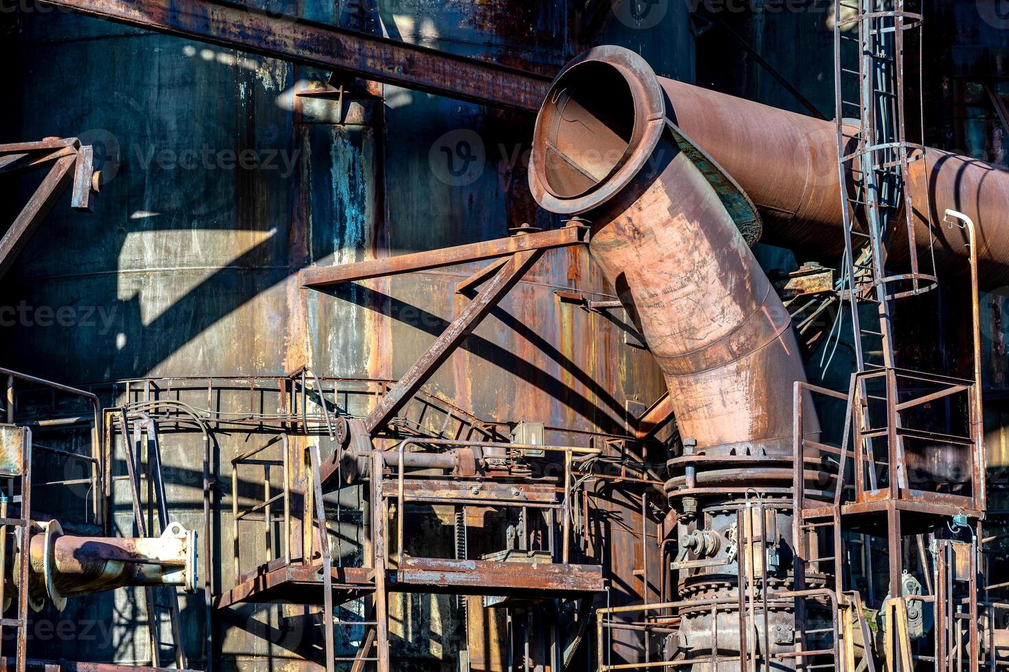 Rusty industrial pipes and metal structures casting shadows on a factory wall photo