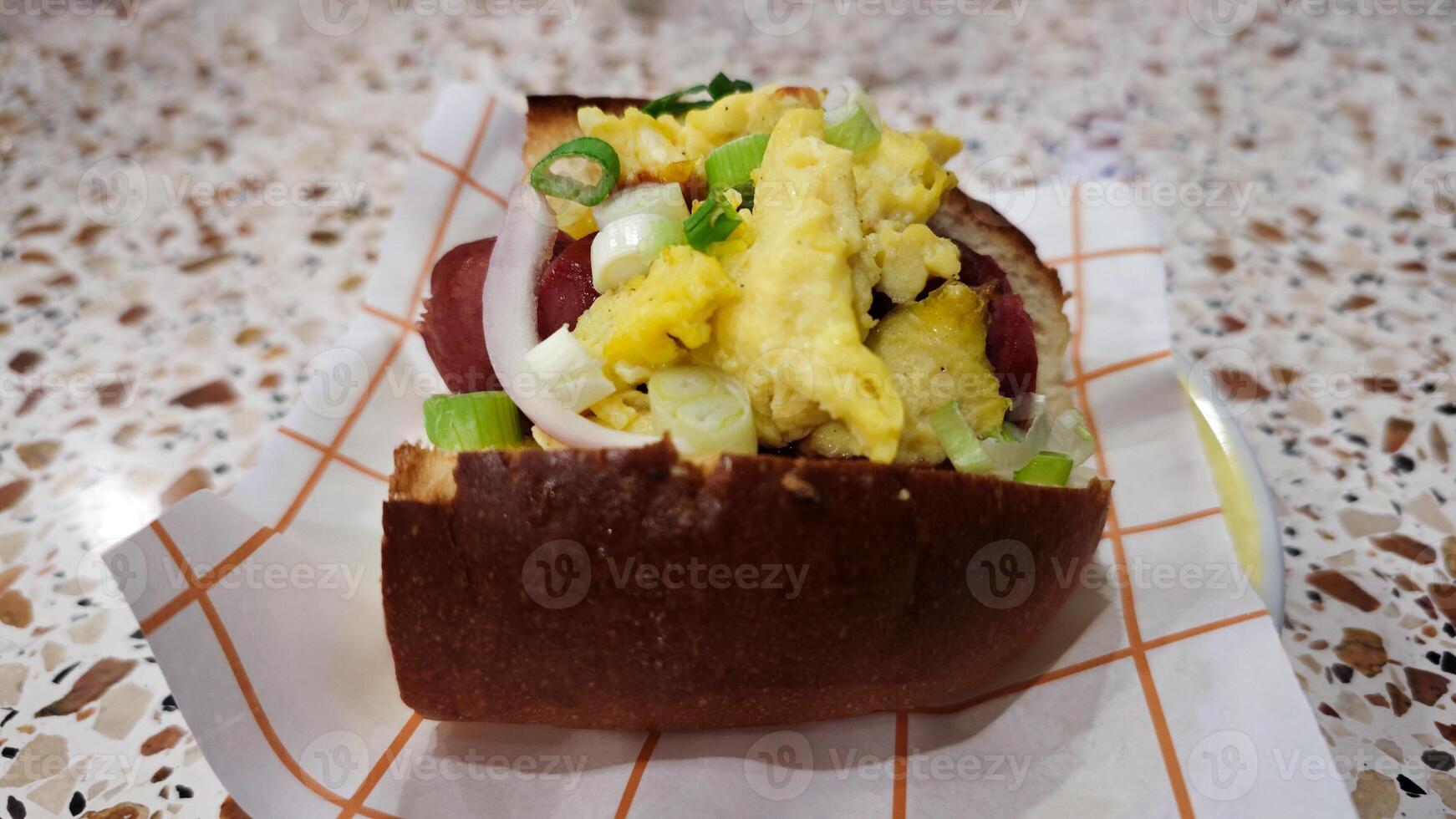 Scrambled egg breakfast sandwich with sausage, green onions, and onions on a soft bun, served on a patterned countertop, perfect for a quick morning bite. photo