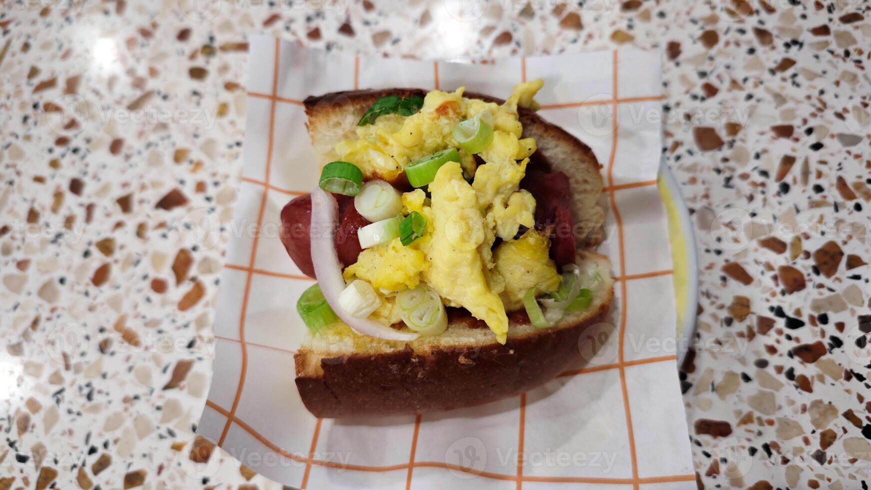 Scrambled egg breakfast sandwich with sausage, green onions, and onions on a soft bun, served on a patterned countertop, perfect for a quick morning bite. photo
