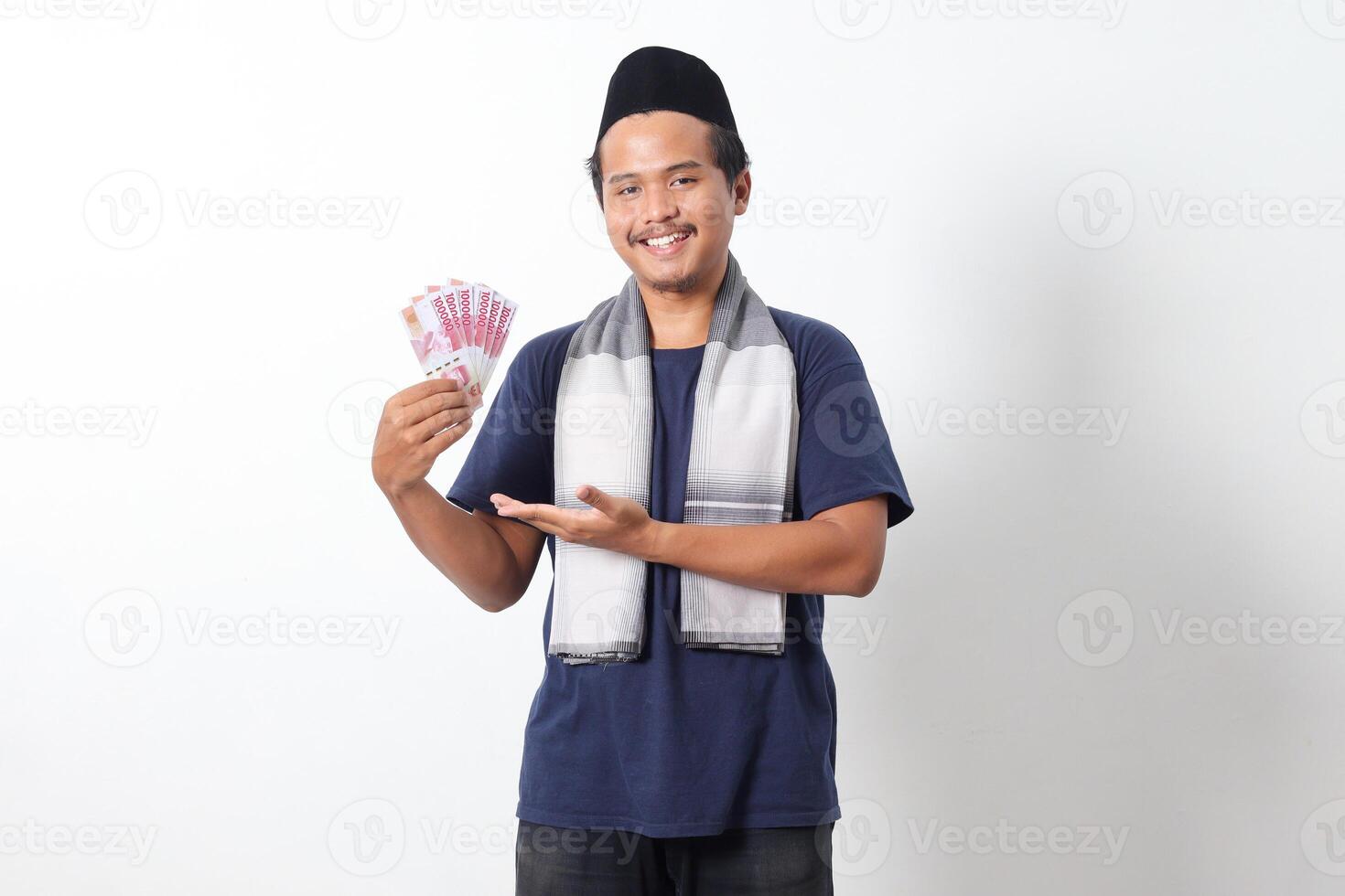 Portrait of frustrated Asian muslim man wearing sarung scarf showing one hundred thousand rupiah while pointing to the side. Financial and investment concept. Isolated image on white background photo