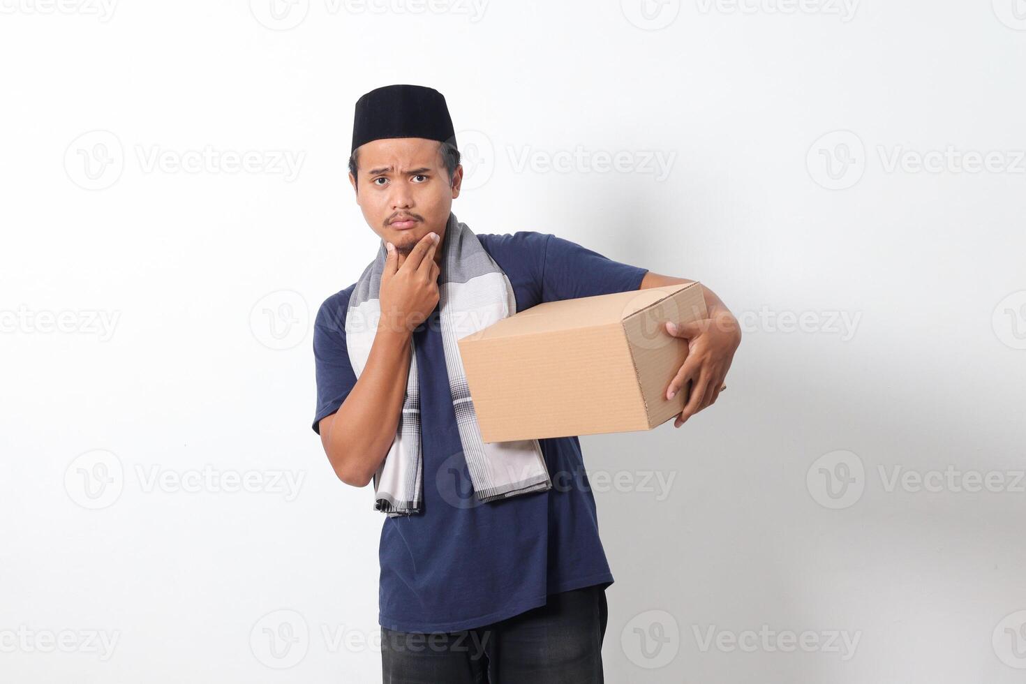 Portrait of confused Asian muslim man wearing sarung scarf and skullcap thinking with hand on chin. Isolated on white background photo