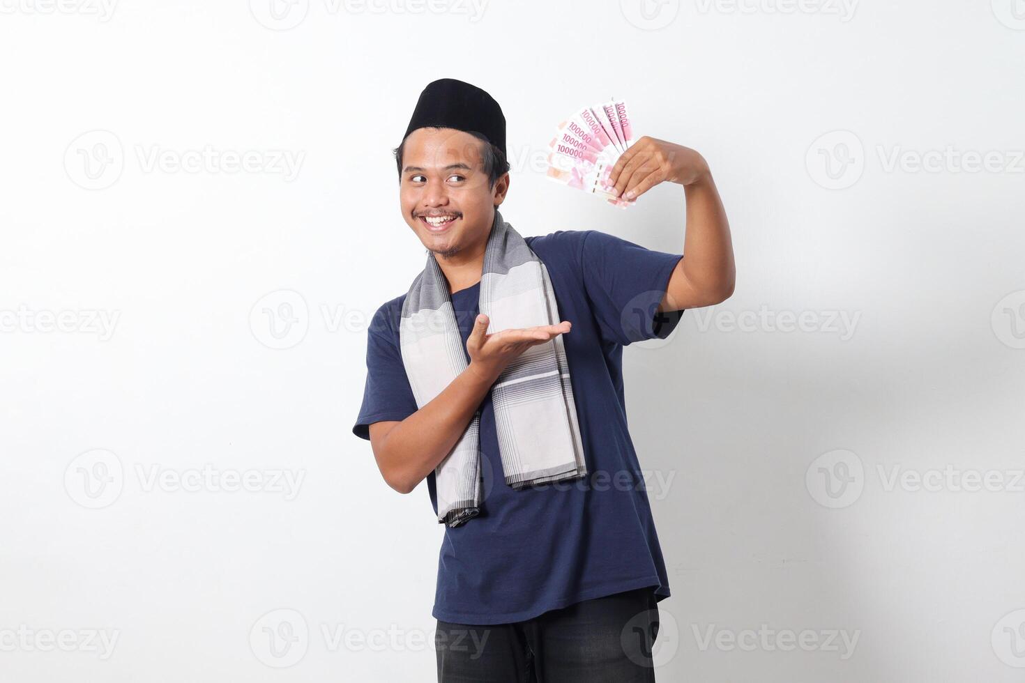 Portrait of frustrated Asian muslim man wearing sarung scarf showing one hundred thousand rupiah while pointing to the side. Financial and investment concept. Isolated image on white background photo