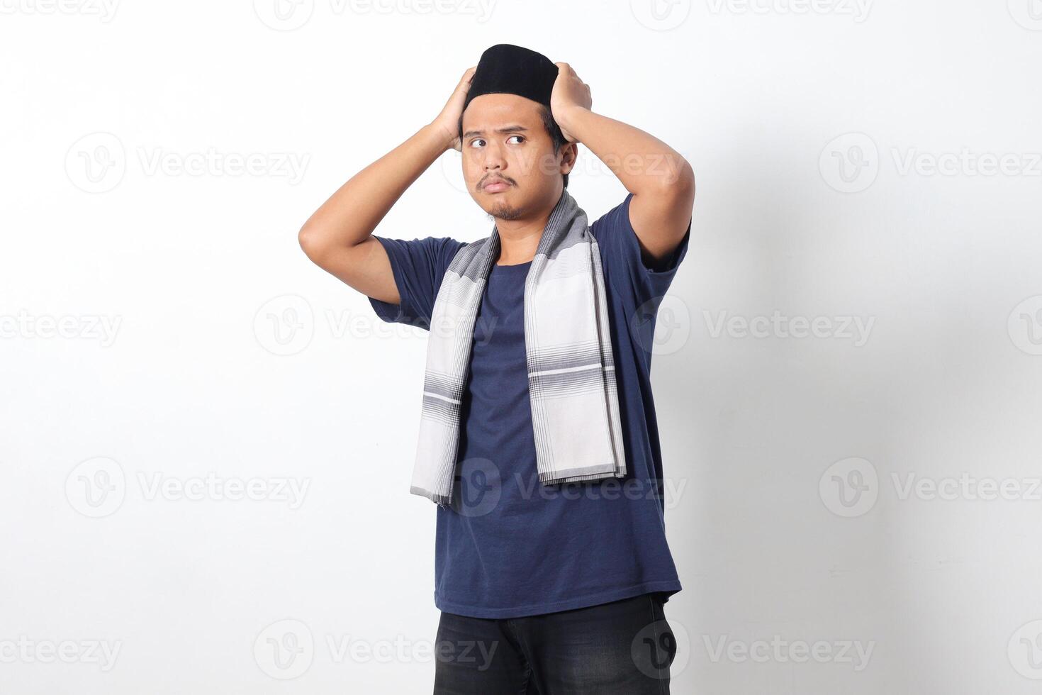 Portrait of excited Asian muslim man wearing sarung scarf trying to adjust his songkok or peci or black skullcap. Isolated image on white background photo