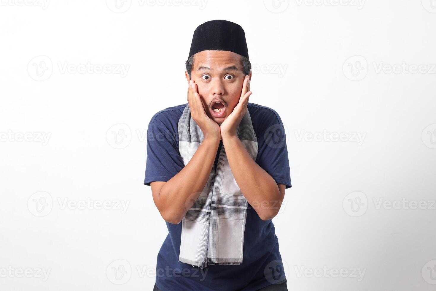 Portrait of scared Asian muslim man wearing sarung scarf looking at camera with shocked eyes and holding his head. Wow face expression. Isolated image on white background photo