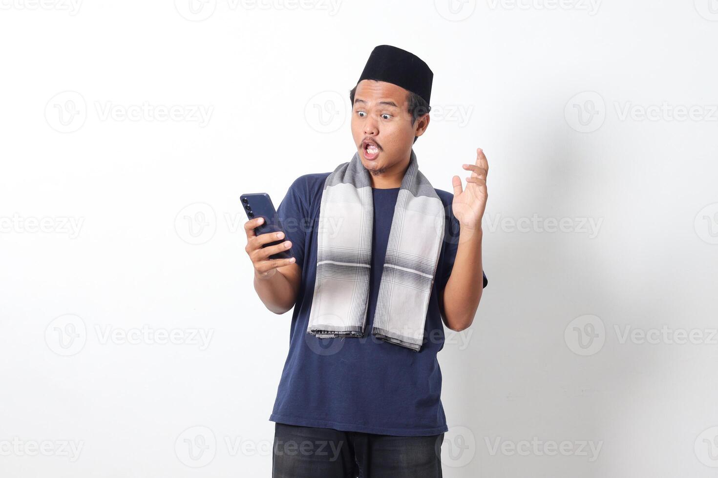 Portrait of upset Asian muslim man wearing sarung scarf and skullcap, holding mobile phone and showing shocked expression. Isolated on white background photo