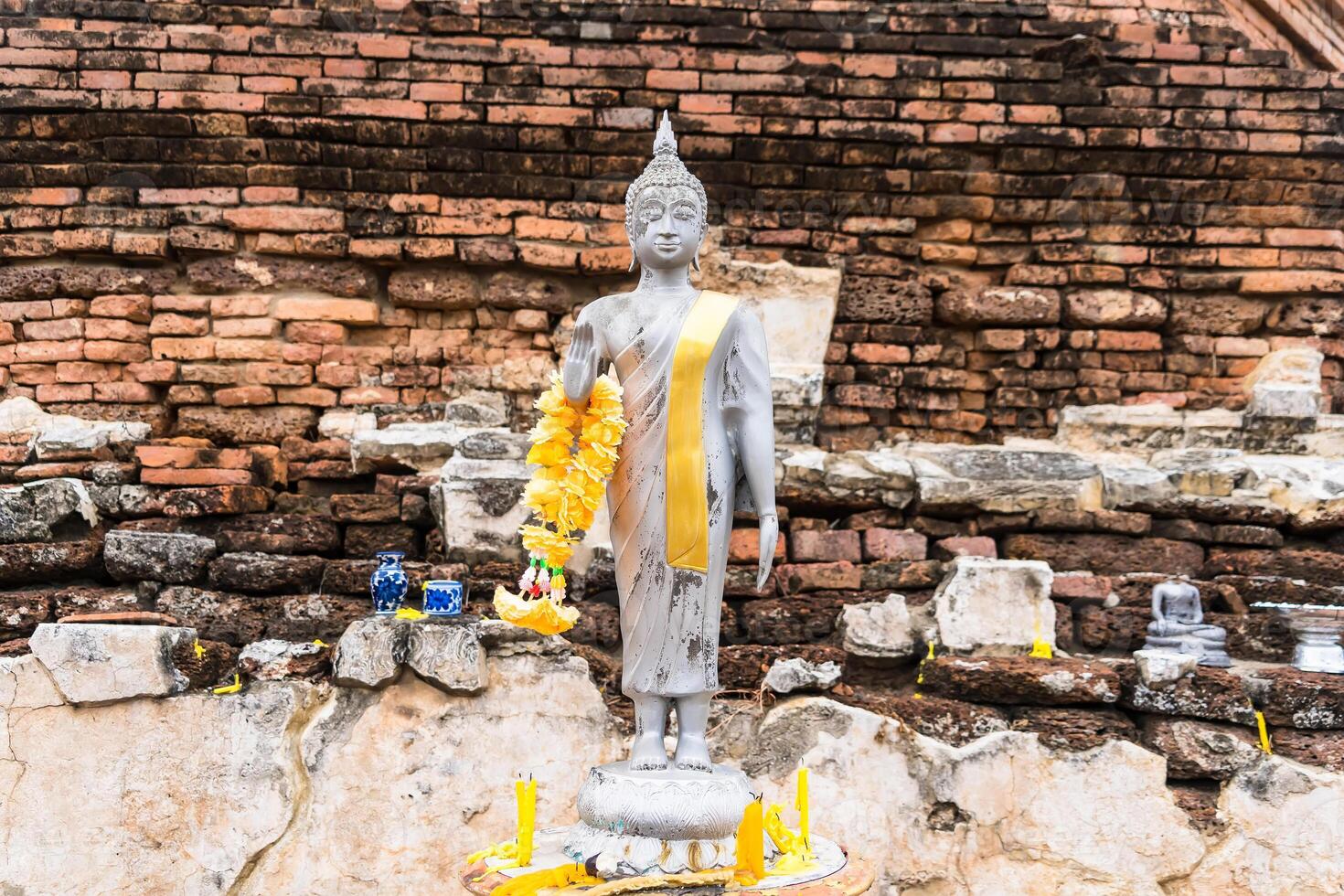 Serene Buddha Figure Draped in Yellow Garland, Set Against a Rustic Brick Background at Ayutthaya, Thailand. photo