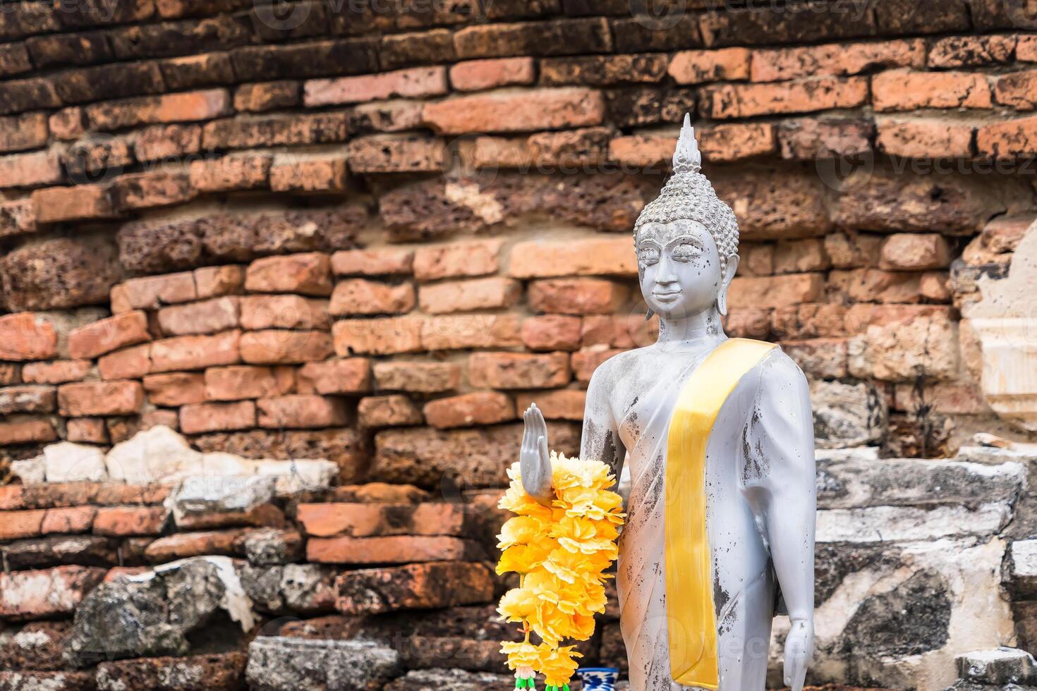 Serene Buddha Figure Draped in Yellow Garland, Set Against a Rustic Brick Background at Ayutthaya, Thailand. photo