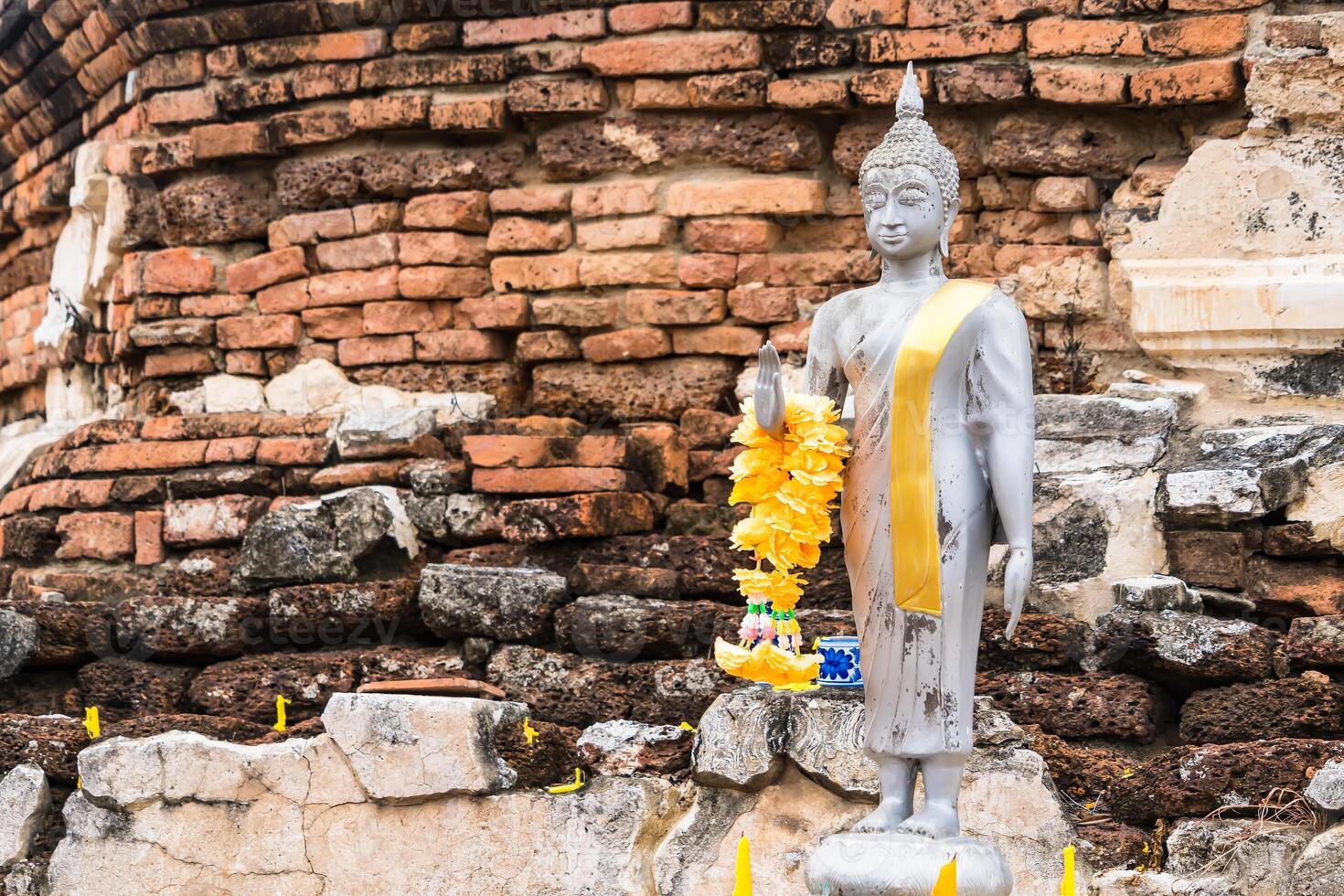 Serene Buddha Figure Draped in Yellow Garland, Set Against a Rustic Brick Background at Ayutthaya, Thailand. photo