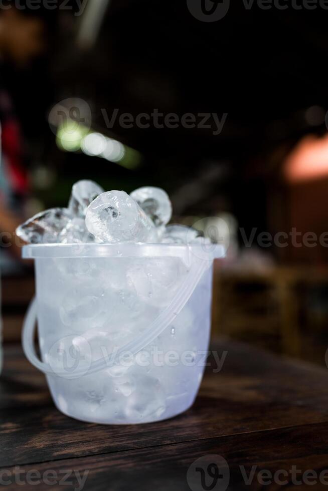 Transparent plastic bucket with ice cube on a table photo