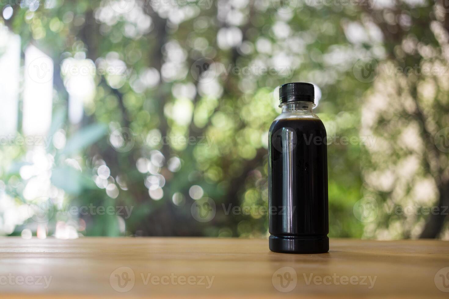 Black coffee in a bottle with bottle. Cold summer drink on a nature background. photo