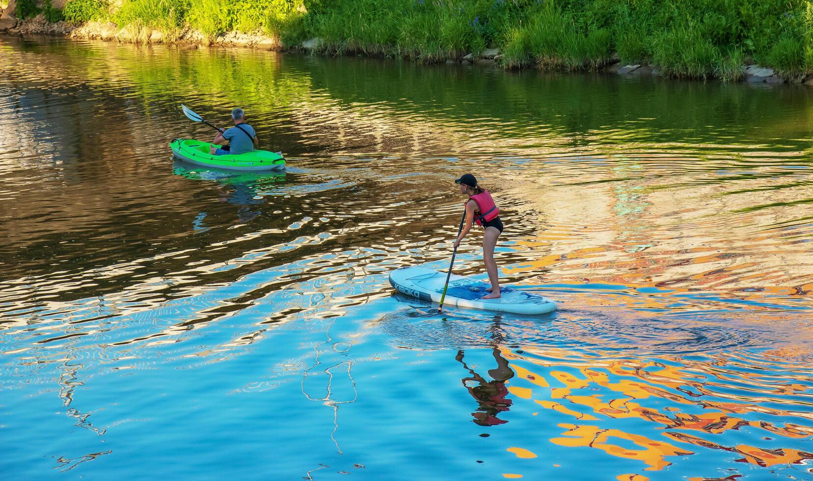 Nitra, Slovakia - 06.15.2022 A young girl and a middle-aged man are sailing in different canoes on the Nitra river. photo