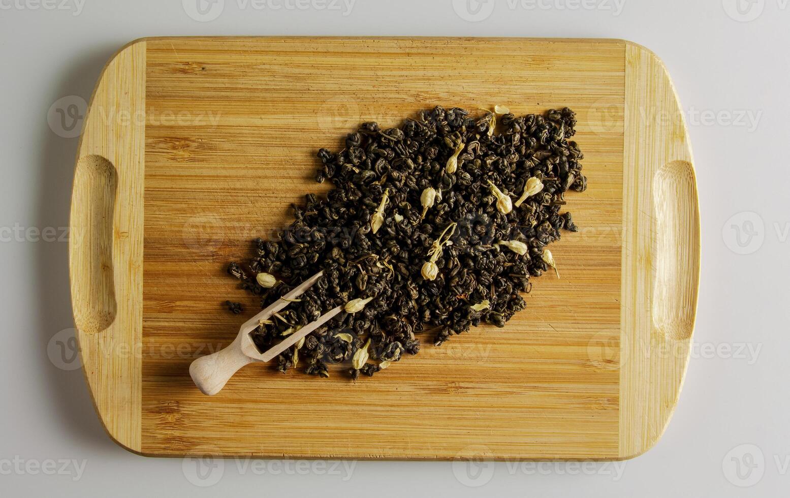 Green dry tea with jasmine flowers on a wooden board and a wooden spoon dispenser. Background and texture of dry tea. photo