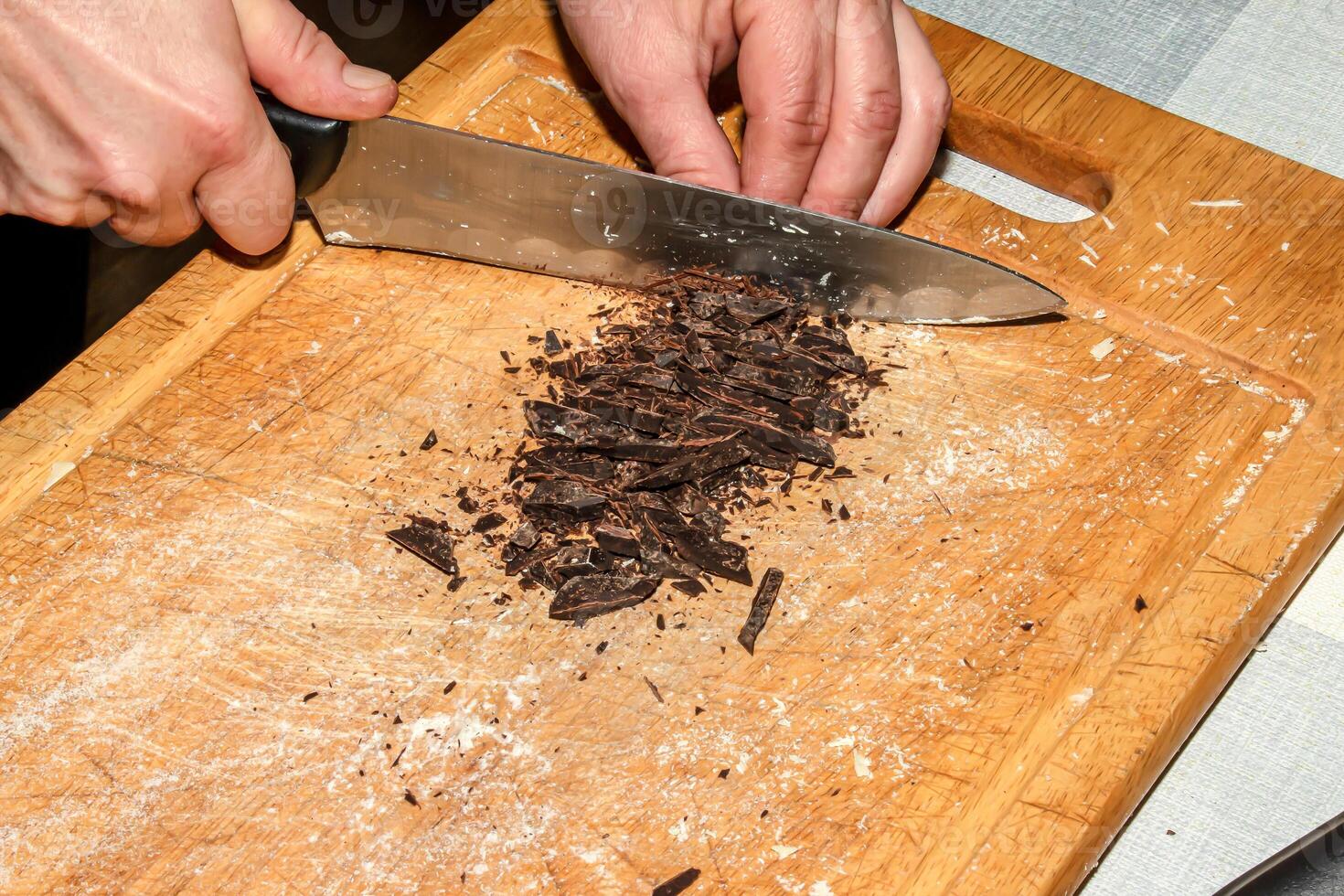 The hands of the cook crush the grated cocoa with a knife on a wooden kitchen board to make chocolate. photo